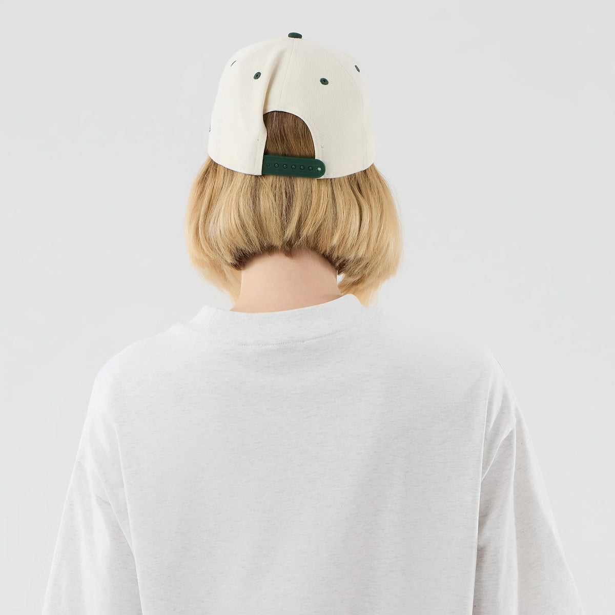 New Era New York Yankees MLB Arch Graphic Pastel Grey Oversized T-Shirt, back view on a model with short blonde hair wearing a light-coloured cap, highlighting the relaxed fit of the plain pastel grey shirt with a rounded neckline.