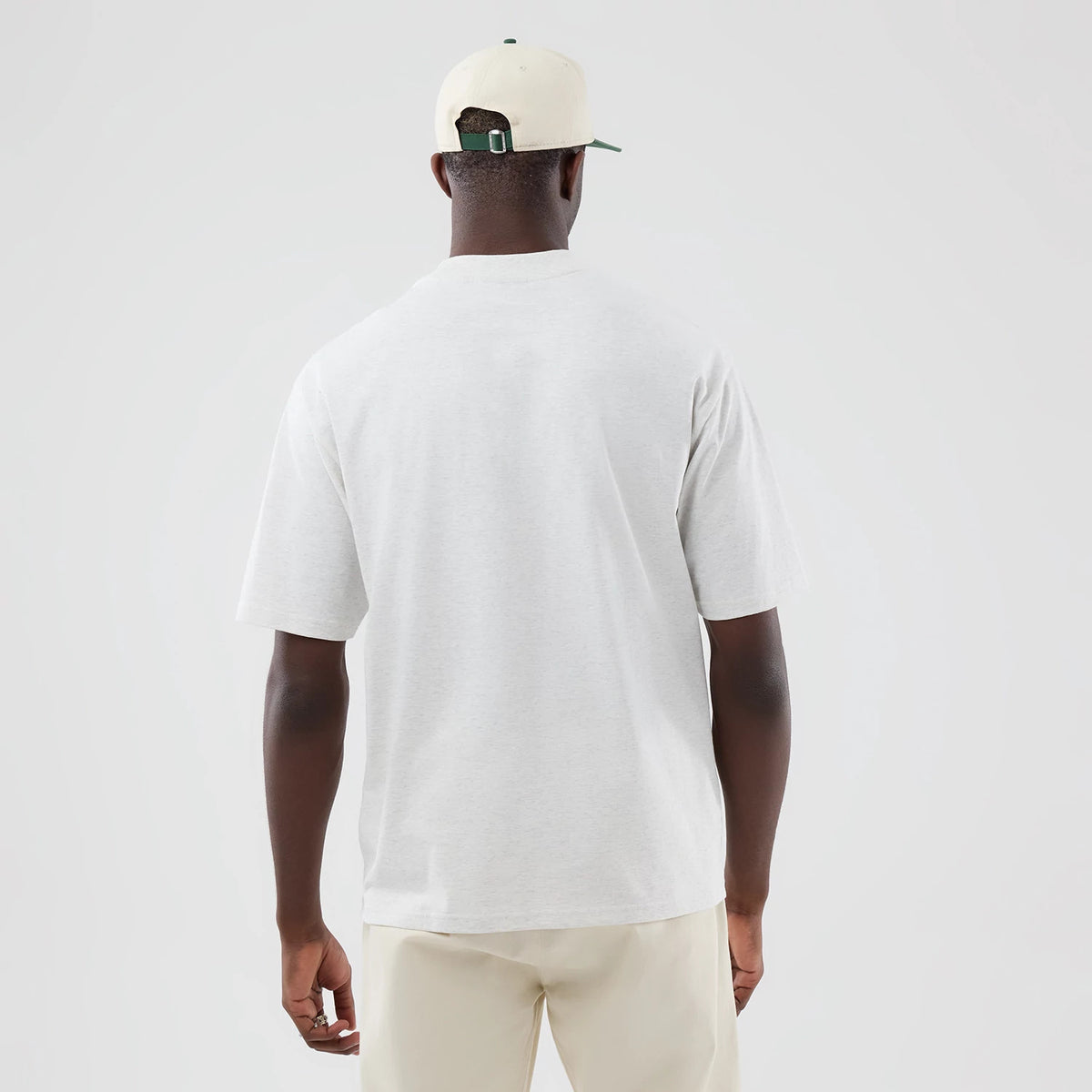 New Era New York Yankees MLB Arch Graphic Pastel Grey Oversized T-Shirt, back view on a model wearing a neutral cap and light trousers, showing a plain, loose fit pastel grey back with short sleeves that extend to the mid-upper arm.