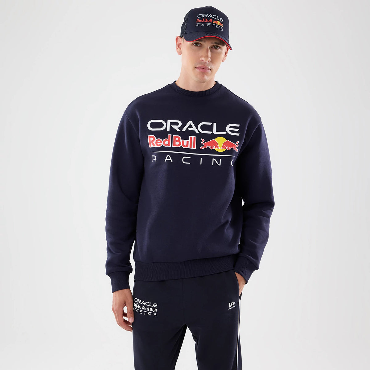 New Era Red Bull Racing Dark Blue Oversized Crew Neck Sweater, front view on a model with a coordinating team cap, featuring Oracle Red Bull Racing lettering and emblem prominently across the chest, with ribbed cuffs and hem for a relaxed fit.
