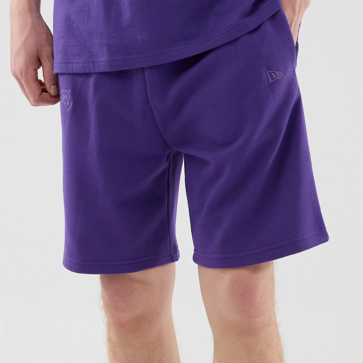 New Era LA Lakers NBA League Essential Purple Oversized Shorts, on-model view showing the relaxed fit purple shorts with an embroidered New Era logo on the left leg, a Lakers logo below the waistband, and styled casually with a matching purple top.