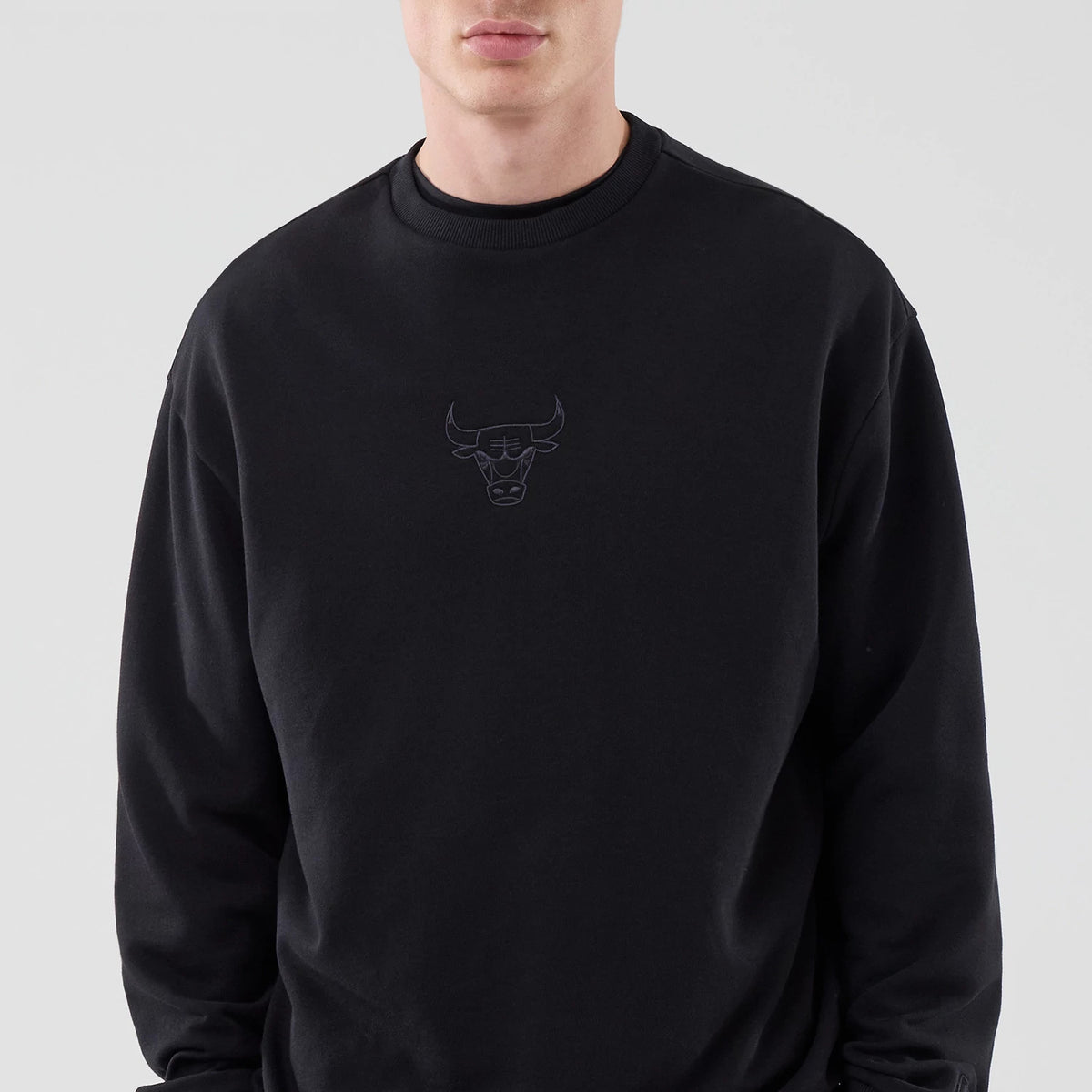 New Era Chicago Bulls NBA League Essential Black Oversized Crew Neck Sweater, front view on a model showing the black embroidered Bulls logo on the chest, with a ribbed collar and relaxed fit enhancing the casual style.