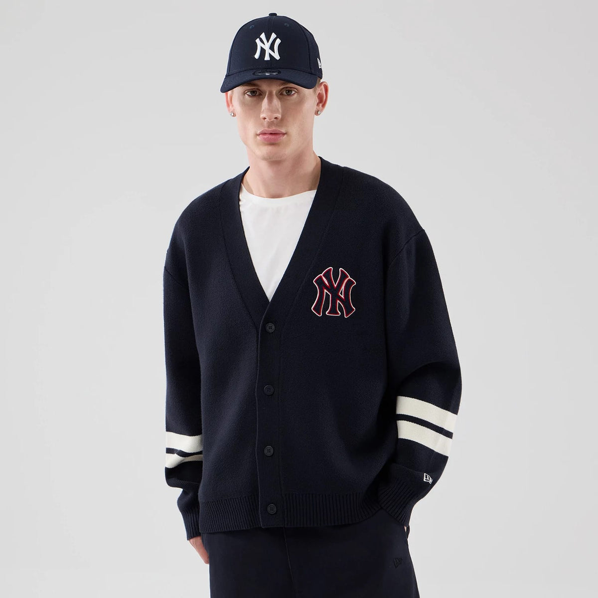 New Era New York Yankees MLB Knit Navy Cardigan, front view on a model featuring the team logo in red and white embroidery on the left chest, button-up fastening, and white-striped on the sleeves, styled with a matching cap.