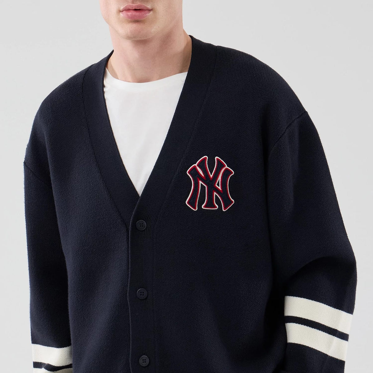 New Era New York Yankees MLB Knit Navy Cardigan, front view on a model with a white shirt underneath, featuring the prominent embroidered NY logo in red outlined in white on the left chest, and striped on the sleeve.