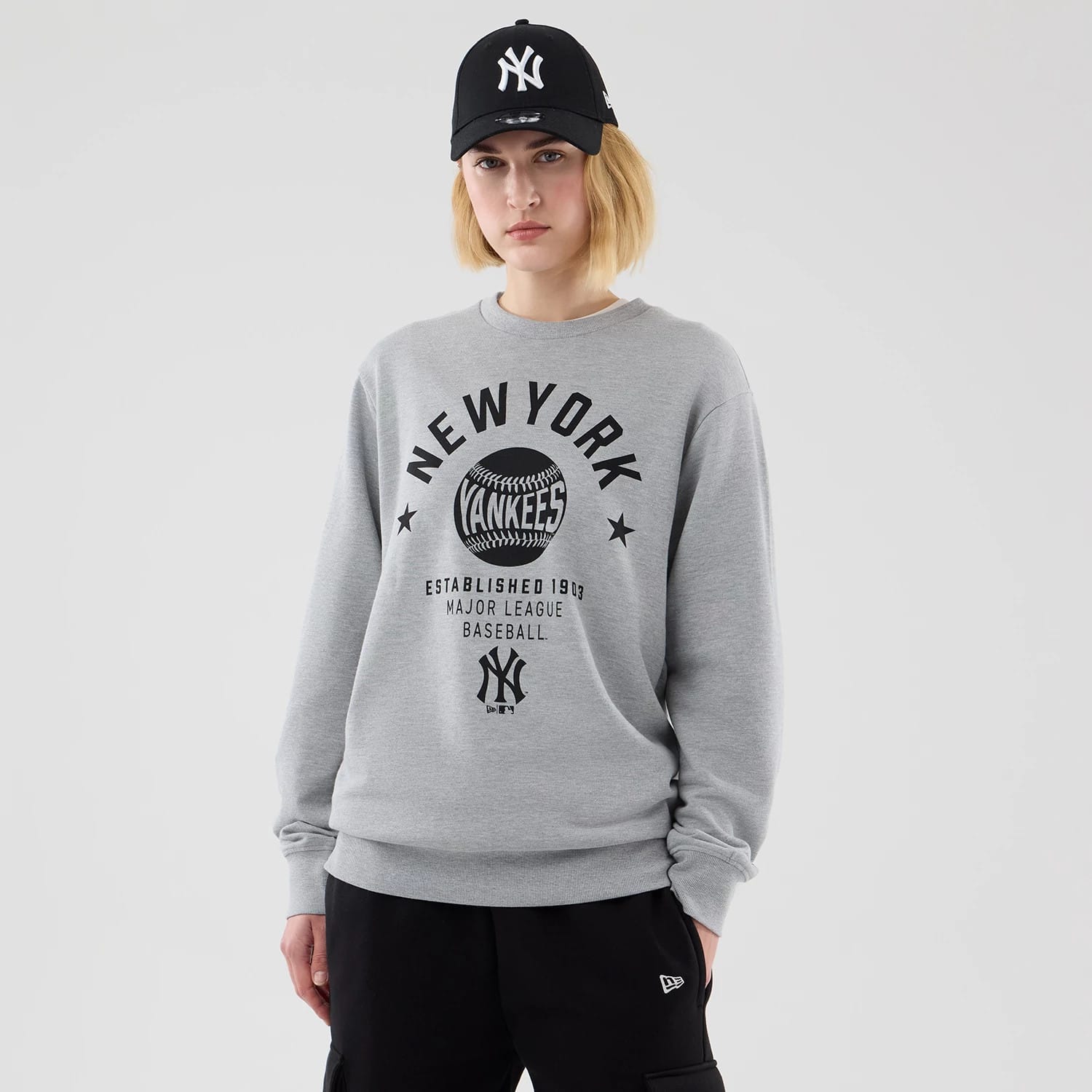 New Era New York Yankees MLB Graphic Grey Oversized Crew Neck Sweater, front view on a model showing a large black and white Yankees baseball graphic across the chest, with 'NEW YORK' lettering above and 'ESTABLISHED 1903' below.