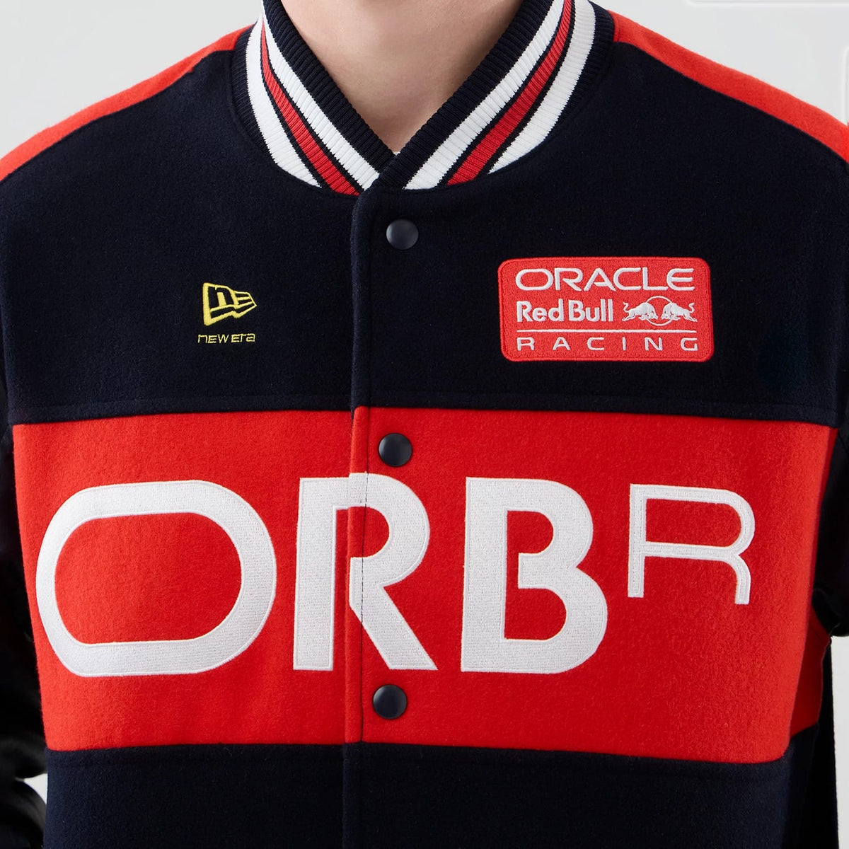 New Era Red Bull Racing wordmark Dark Blue Varsity Jacket, front view showing a red and dark blue colour block design, a white embroidered ORBR across the chest, a yellow embroidered New Era logo on the left side.