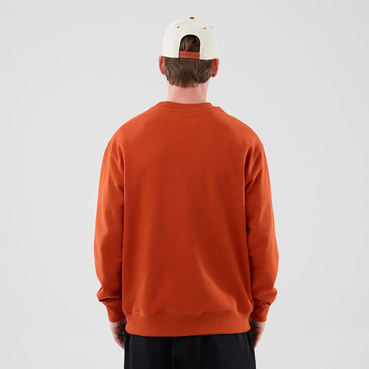 New Era New York Yankees MLB Arch Graphic Orange Oversized Crew Neck Sweater, back view on a model wearing a white cap with a red adjustable strap, featuring a relaxed fit with dropped shoulders and ribbed cuffs and hem.