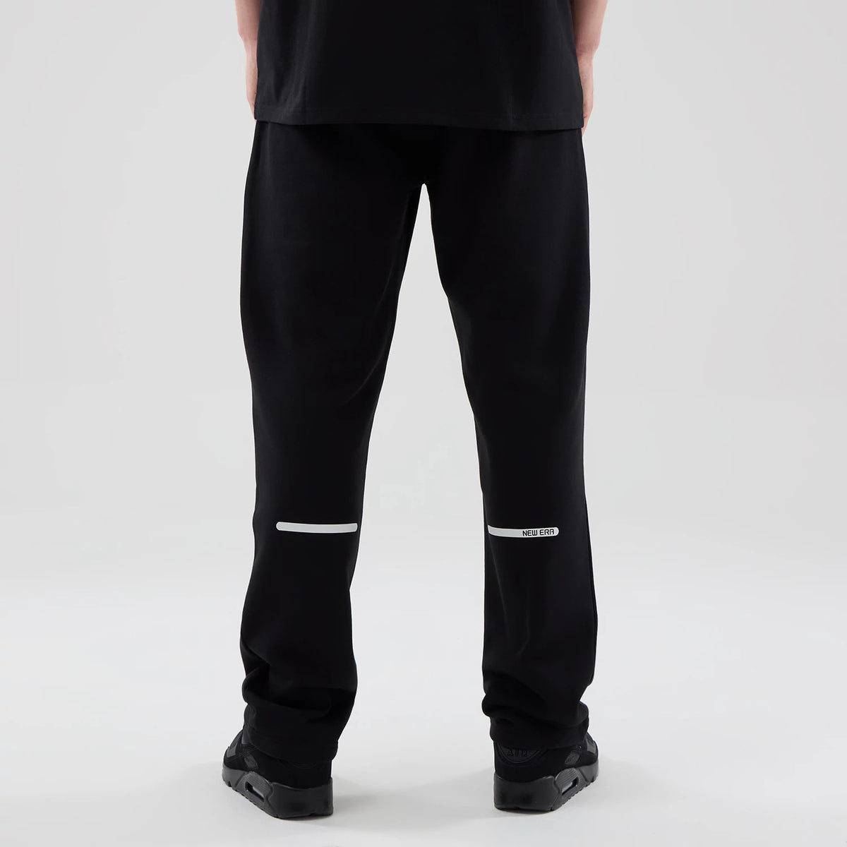 New Era Tech Reflective Black Straight Leg Joggers, back view on a model showing reflective white stripe across the lower legs, with a New Era logo on the right, and a loose fit design around the ankles.