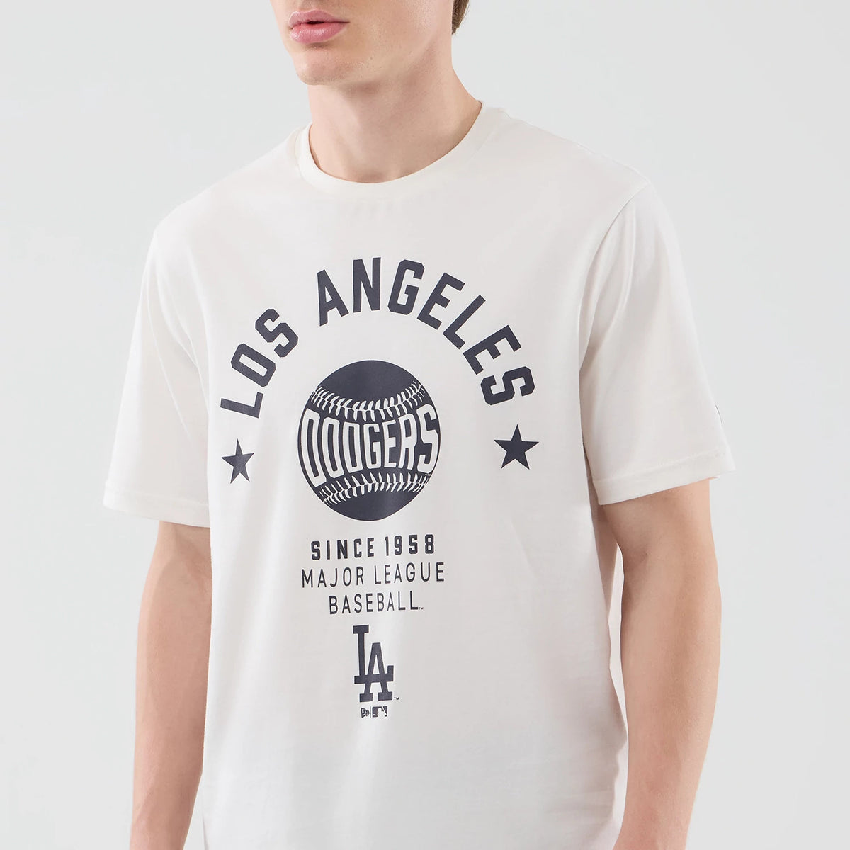 New Era LA Dodgers MLB Graphic Open White T-Shirt, front view on a model displaying a large printed graphic with Los Angeles and Dodgers inside a baseball design, two stars flanking the graphic, and Since 1958 Major League Baseball text below.