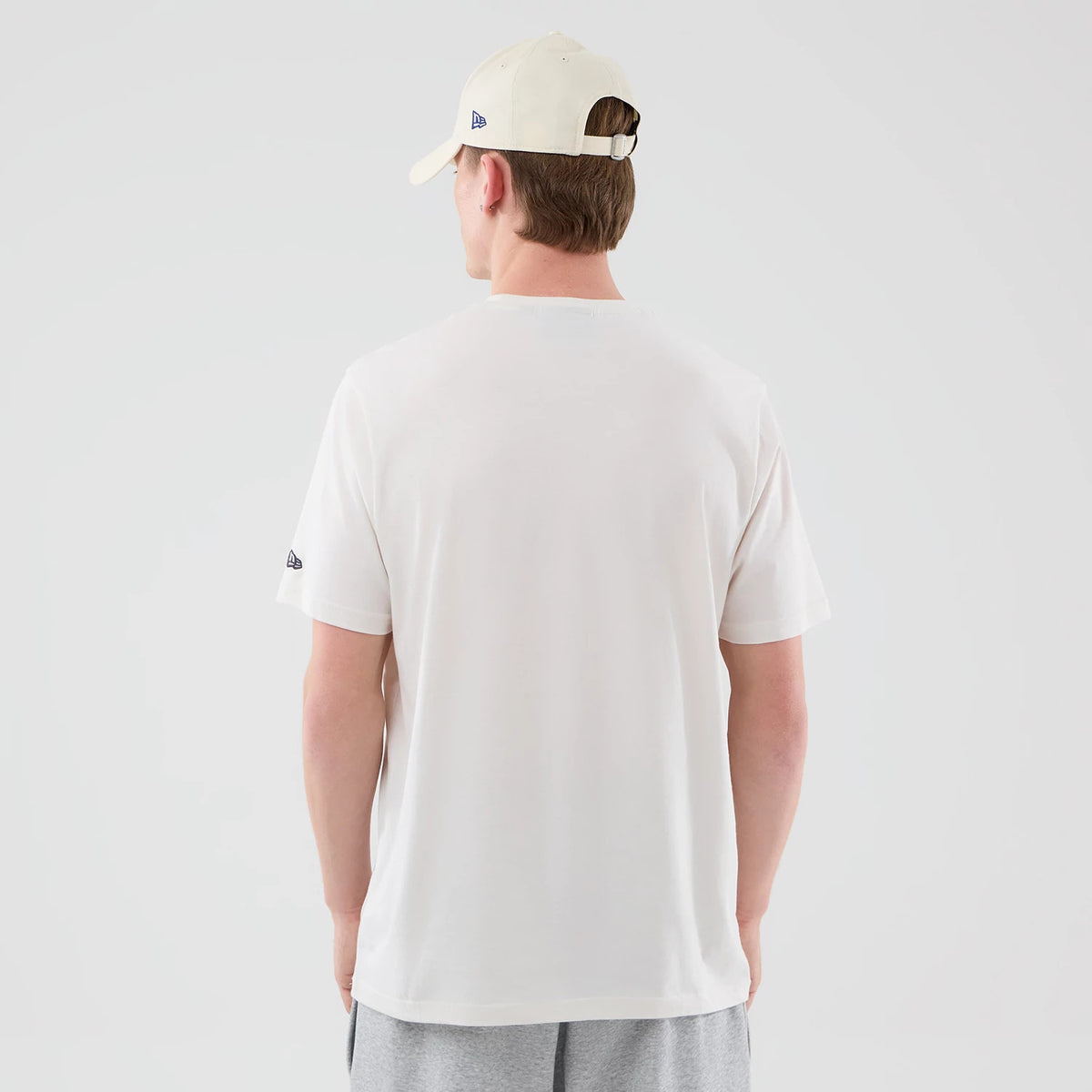 New Era LA Dodgers MLB Graphic Open White T-Shirt, back view on a model wearing a light-coloured cap and grey shorts, featuring a clean white back without graphics, and an embroidered New Era logo on the left sleeve.