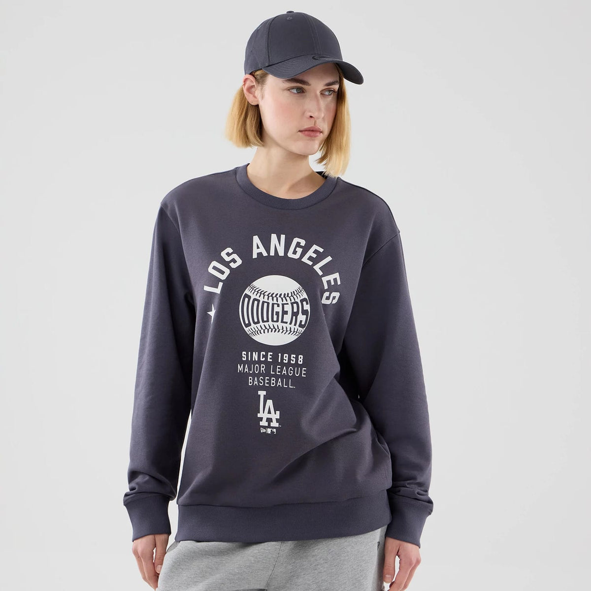 New Era LA Dodgers MLB Graphic Grey Oversized Crew Neck Sweater, front view on a model featuring a prominent white Los Angeles Dodgers graphic with baseball and text design across the chest, showcasing ribbed cuffs and a relaxed fit.