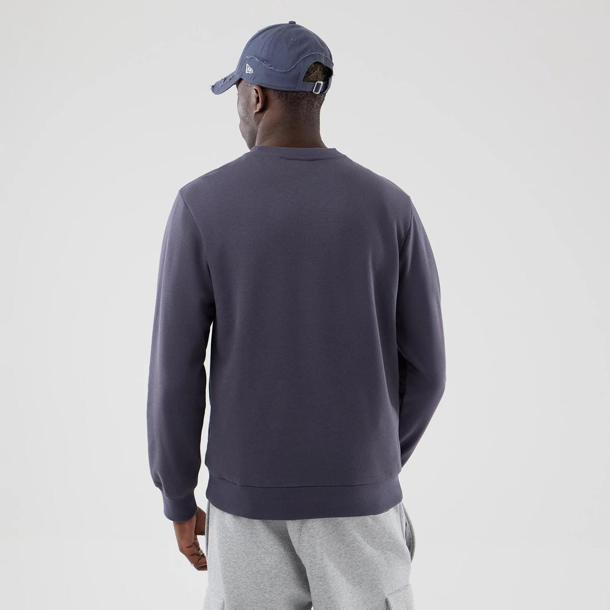 New Era LA Dodgers MLB Graphic Grey Oversized Crew Neck Sweater, back view on a model with a grey cap, showing the plain grey fabric with a relaxed fit and ribbed cuffs, paired with light grey casual jogging pants.