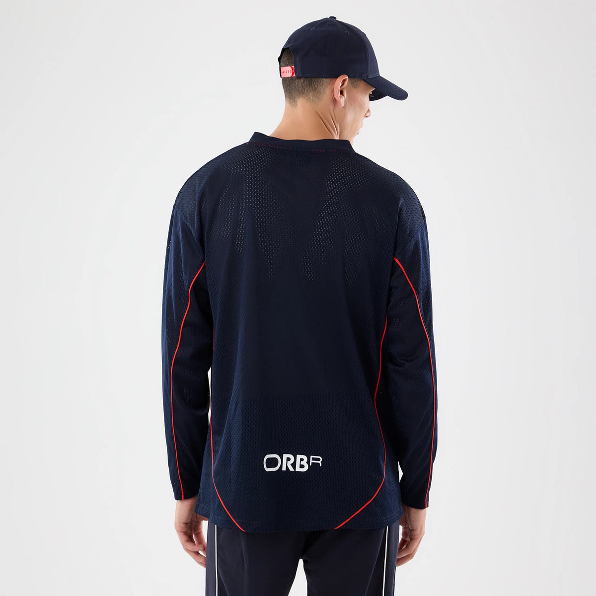New Era Red Bull Racing Dark Blue Hockey Jersey, back view on a model wearing a matching dark blue cap, showing white ORBR lettering near the hem, textured dark blue fabric, and contrasting red piping along the sleeves.