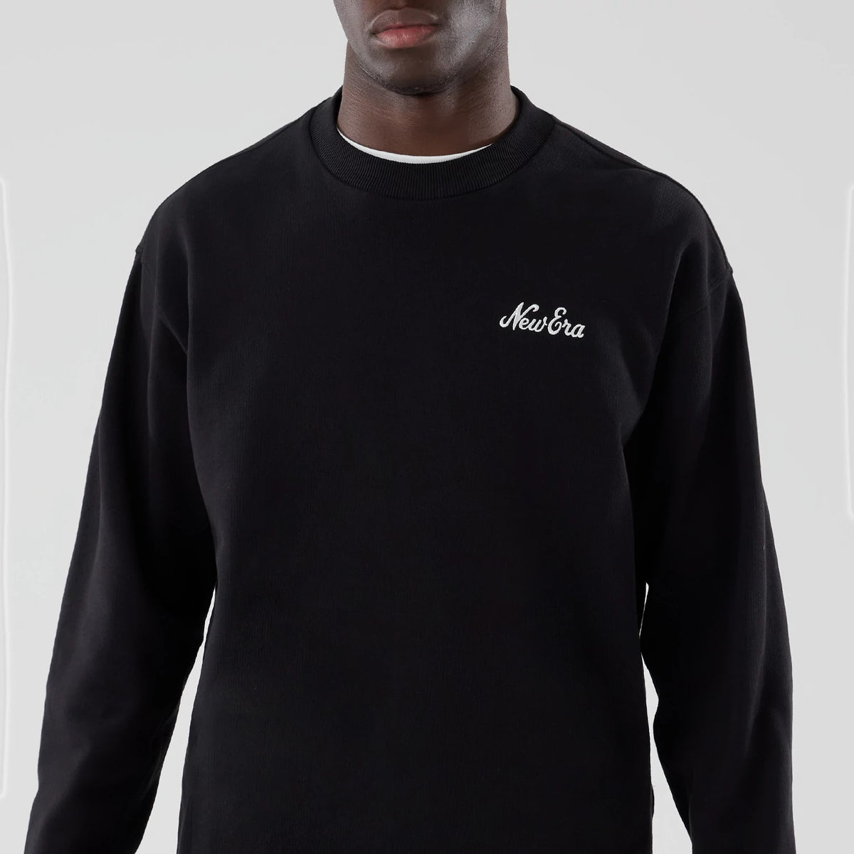New Era Black Oversized Crew Neck Sweater, front view on a model showing the white embroidered New Era logo on the left chest, ribbed crew neck collar, and long sleeves, highlighting the relaxed fit and plain black fabric.