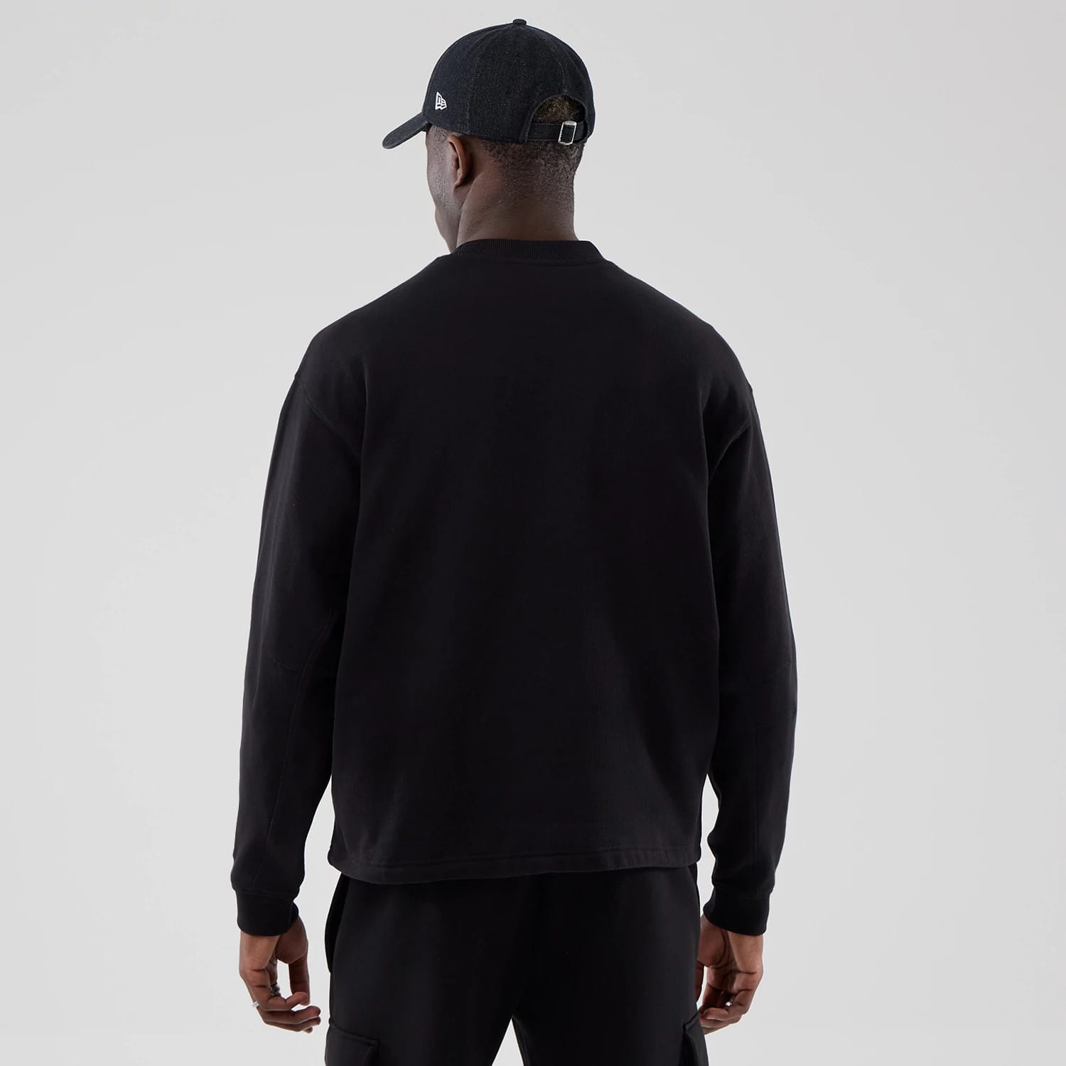 The model is wearing this New Era Oversized Crew Neck Sweater in black. 2