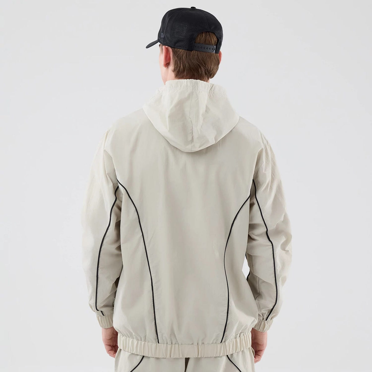 New Era New York Yankees MLB Piping Cream Jacket, back view on a model wearing a black cap, showing the cream jacket with a hood and contrasting black piping running down the sleeves and sides, with elasticated cuffs and waistband.