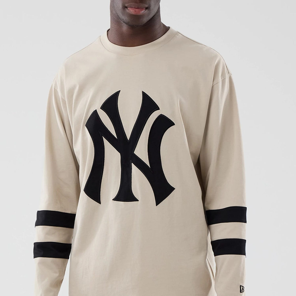 New Era New York Yankees MLB Light Beige Oversized Long Sleeve T-Shirt, front view showing the large black embroidered Yankees logo prominently on the chest, with two black horizontal stripes on each sleeve.