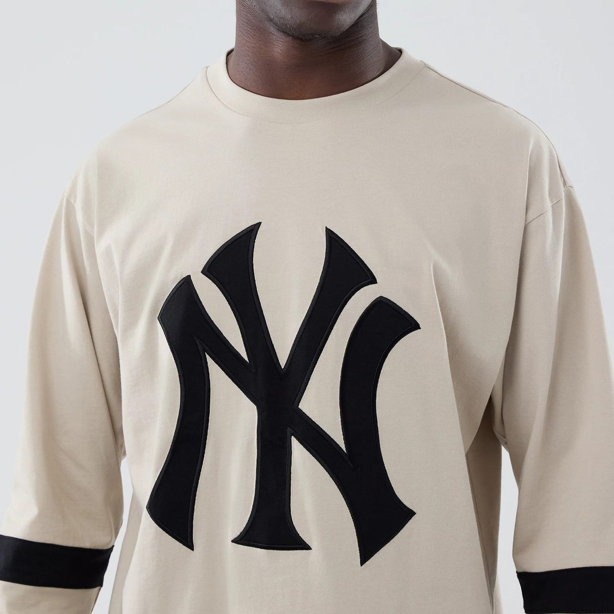 New Era New York Yankees MLB Light Beige Oversized Long Sleeve T-Shirt, front view displaying a large black embroidered Yankees logo centred on the chest, with black stripe around the forearms on both sleeves, worn by a model.