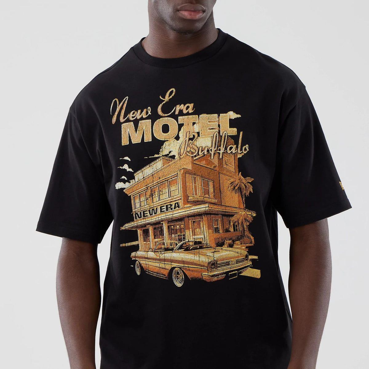 New Era Motor Graphic Black Oversized T-Shirt, front view showing a yellow and brown graphic of a classic car and motel under New Era Motel Buffalo lettering, with a small embroidered New Era logo on the left sleeve.