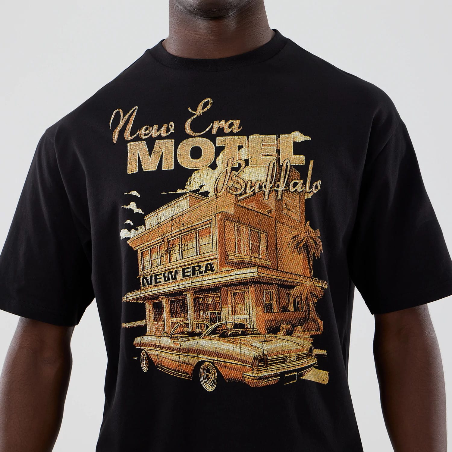 New Era Motor Graphic Black Oversized T-Shirt, front view with a vintage motel graphic featuring a classic car and palm trees, the words New Era Motel Buffalo in gold lettering across the chest.