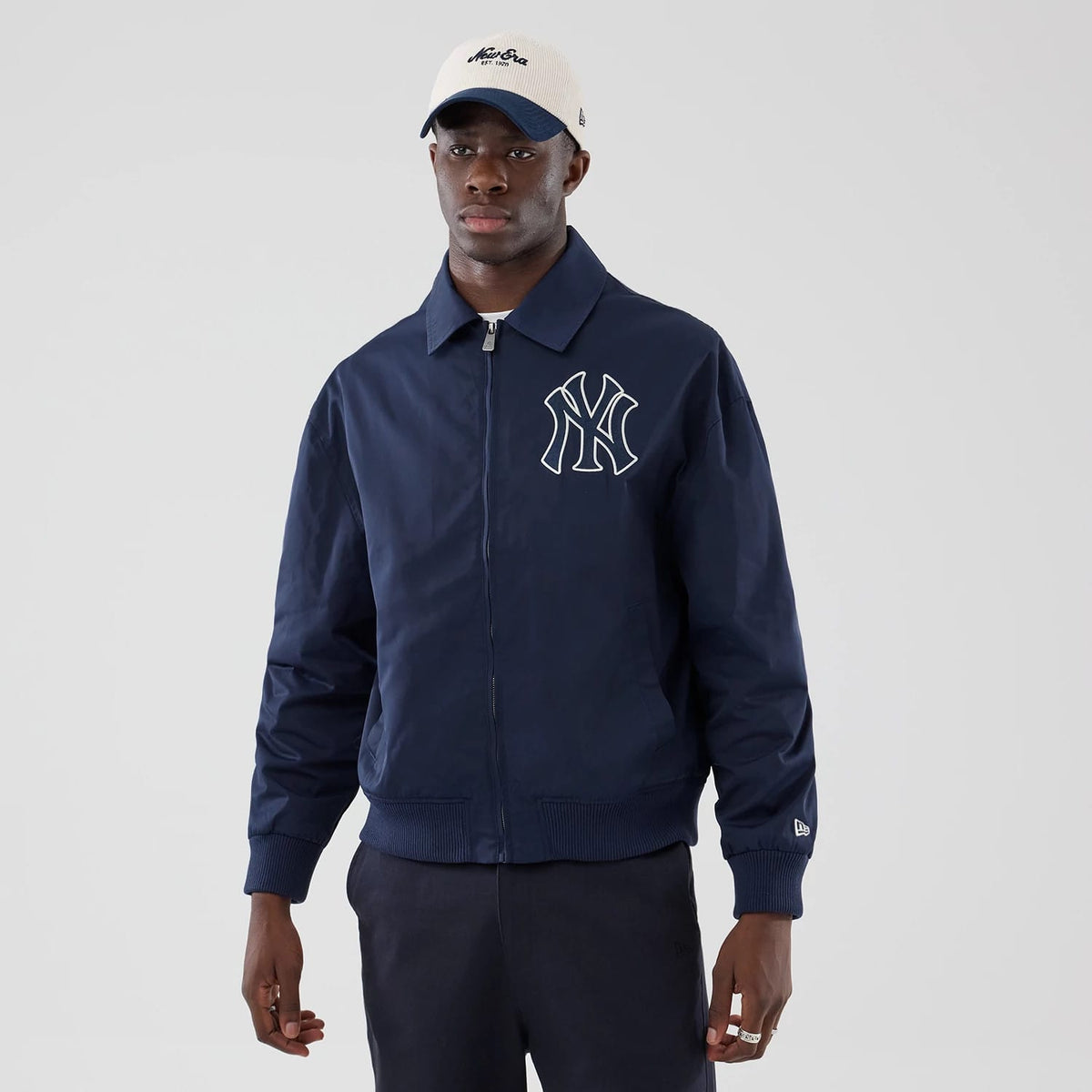 New Era New York Yankees MLB Collared Navy Jacket, front view on a model showing the prominent white embroidered Yankees logo on the chest, a zippered front, and a collared design complemented by the New Era flag on the sleeve.