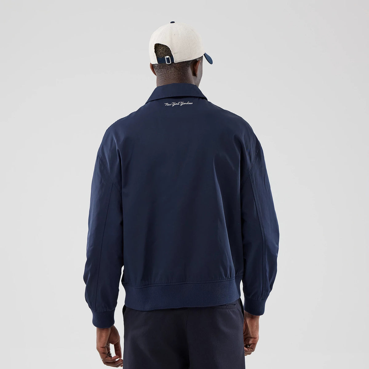 New Era New York Yankees MLB Collared Navy Jacket, back view on a model showing the embroidered New York Yankees lettering at the neck, a dark navy colour throughout, and loose long sleeves offering a classic fit over dark trousers.
