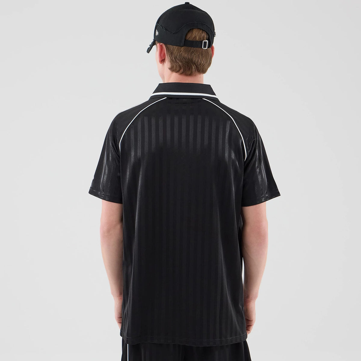 New Era Black Football Jersey T-Shirt, back view on a model featuring vertical pinstripes on the black fabric, white piping along the shoulders and collar, and short sleeves, with the model wearing a matching black cap.