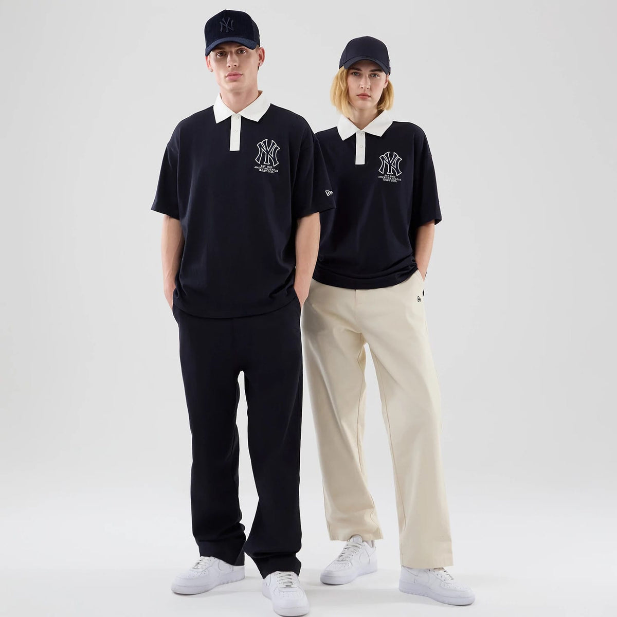 New Era New York Yankees MLB Navy Polo T-Shirt, front view on models showcasing the navy polo with a white collar and embroidered New York Yankees logo on the chest, paired with casual black and beige trousers and matching navy caps.