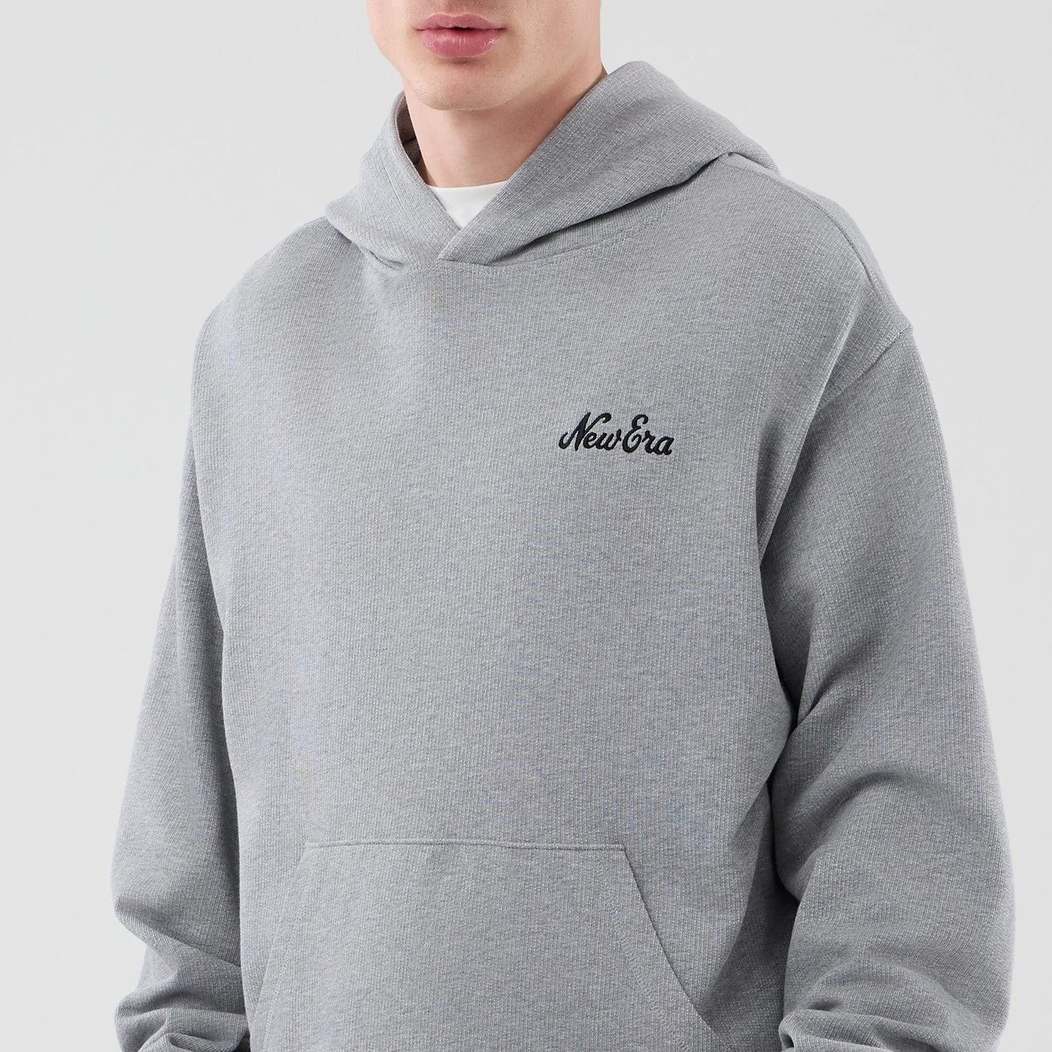 New Era Open Hem Grey Pullover Hoodie, front view showing a black embroidered New Era logo on the left chest, a spacious kangaroo pocket below and the look of the open hem design worn over a white layer on a model.