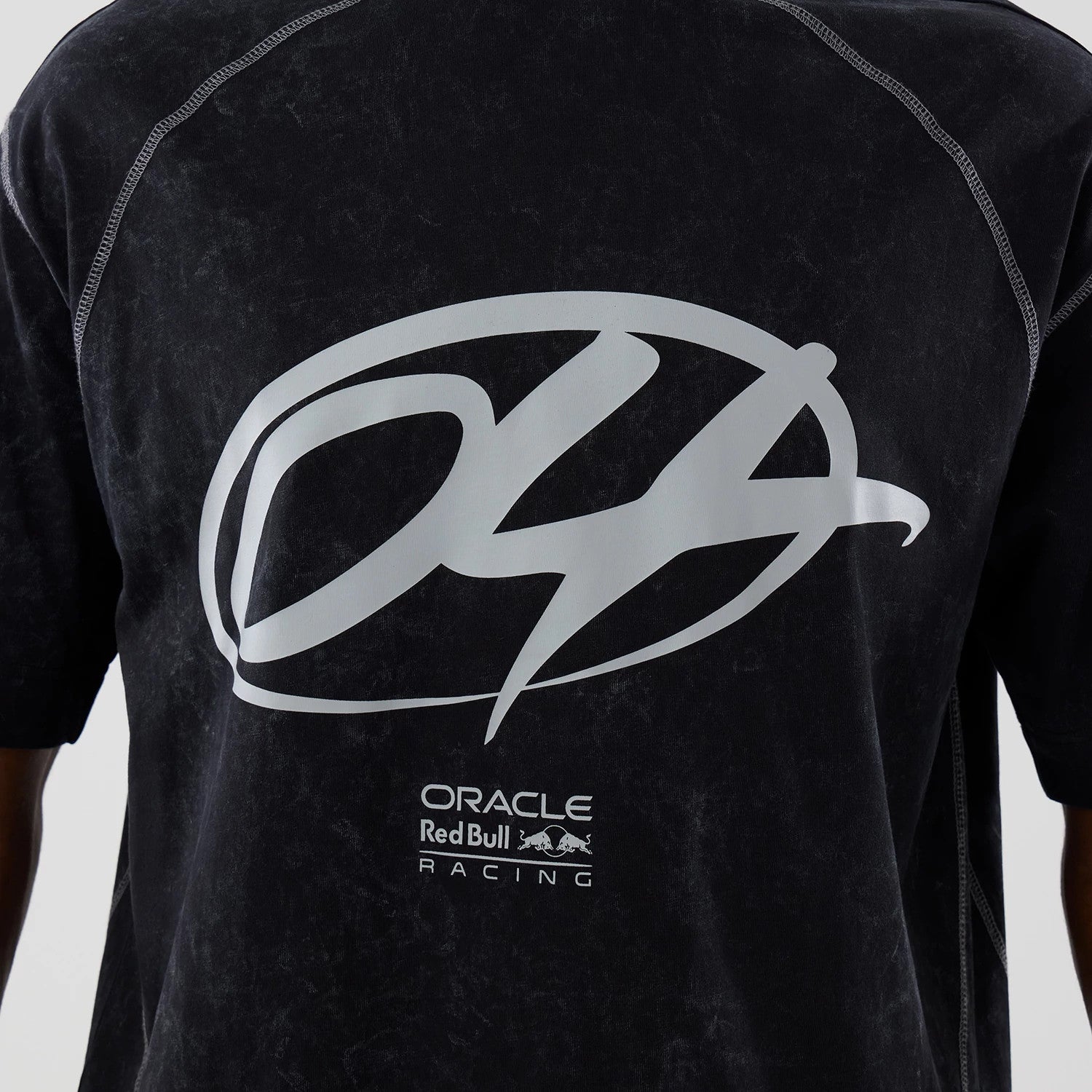 New Era Red Bull Racing Black Drop Shoulder T-Shirt, front view showcasing a large grey printed emblem across the chest, contrast stitching along the shoulders, and a marbled texture on the fabric, worn by a model.