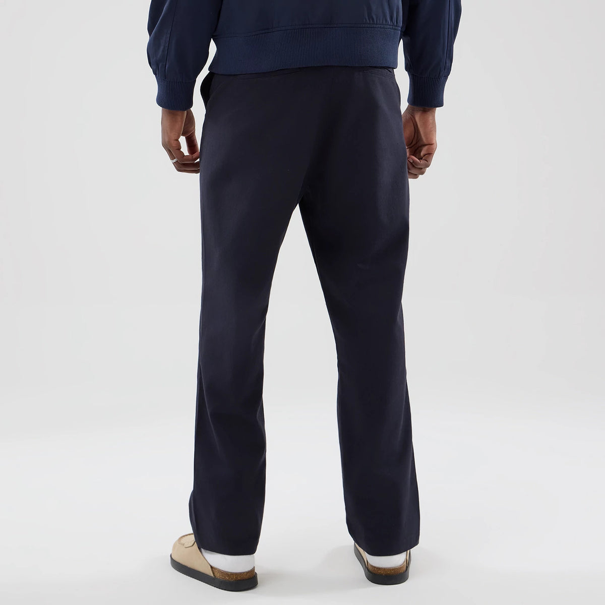 New Era Navy Chino Trousers, rear view on a model showcasing the structured fit and straight leg design, with a clean waistband and fabric finish, complemented by a navy jacket and beige shoes.