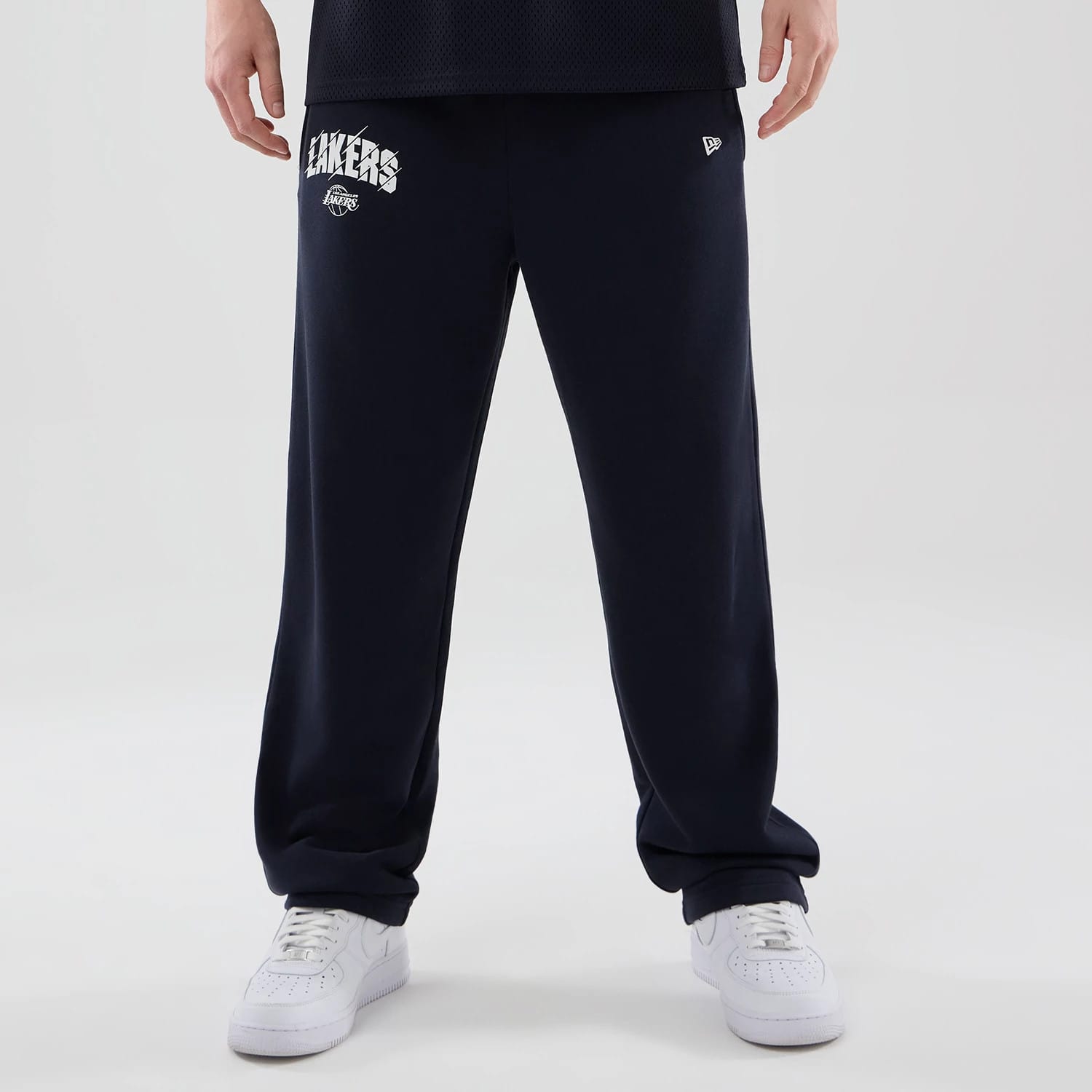New Era LA Lakers NBA Core Plus Navy Straight Leg Joggers, front view on a model with white sneakers, showing the white Lakers lettering and logo on the upper left leg, along with the New Era flag logo on the right side.