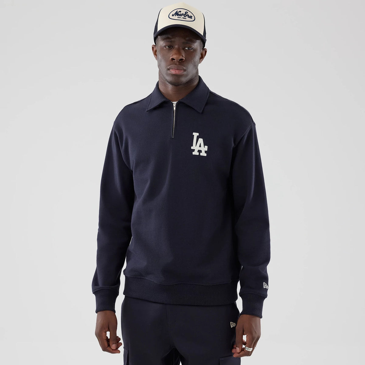 New Era LA Dodgers MLB Navy Oversized 1/4 Zip Sweater, front view on a model with a New Era cap, showing the white LA logo embroidered on the left chest, ribbed cuffs, and the New Era flag logo on the left sleeve.