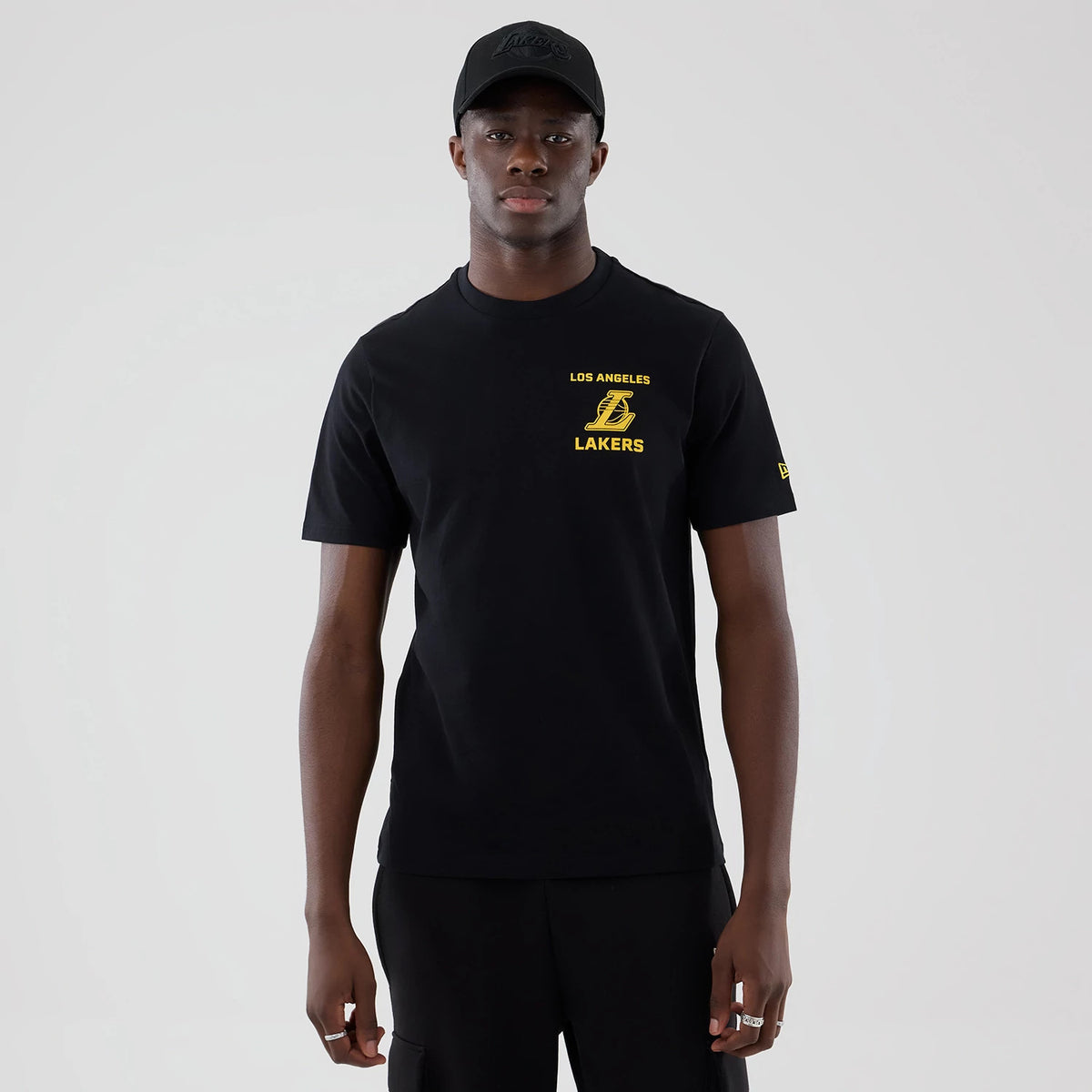 New Era LA Lakers NBA Court Graphic Black T-Shirt, front view on a model styled with a matching black cap, featuring a yellow printed Los Angeles Lakers logo and lettering on the chest, with a yellow New Era logo on the left sleeve.