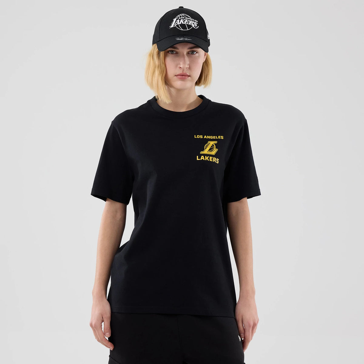 New Era LA Lakers NBA Court Graphic Black T-Shirt, front view on a model also wearing a black cap, featuring a yellow embroidered Los Angeles Lakers logo on the left chest, set against a plain black background.