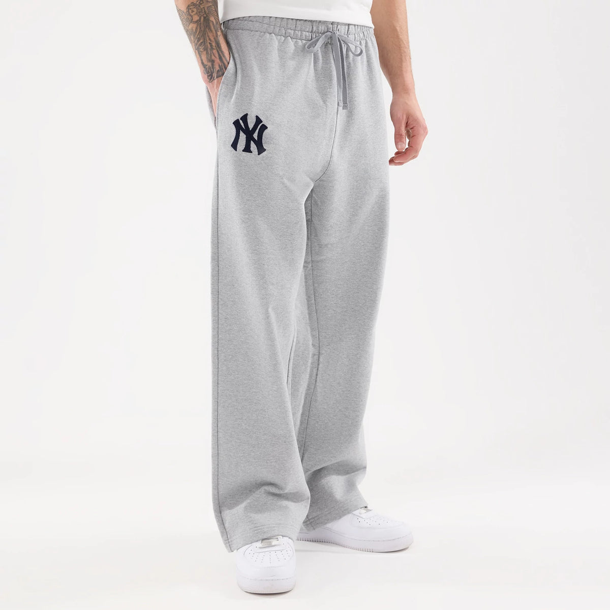 New Era New York Yankees MLB Straight Leg Grey Straight Leg Joggers, front view on a model showing the elasticated waistband with a drawstring, navy embroidered Yankees logo on the left thigh, and the relaxed fit over white trainers.