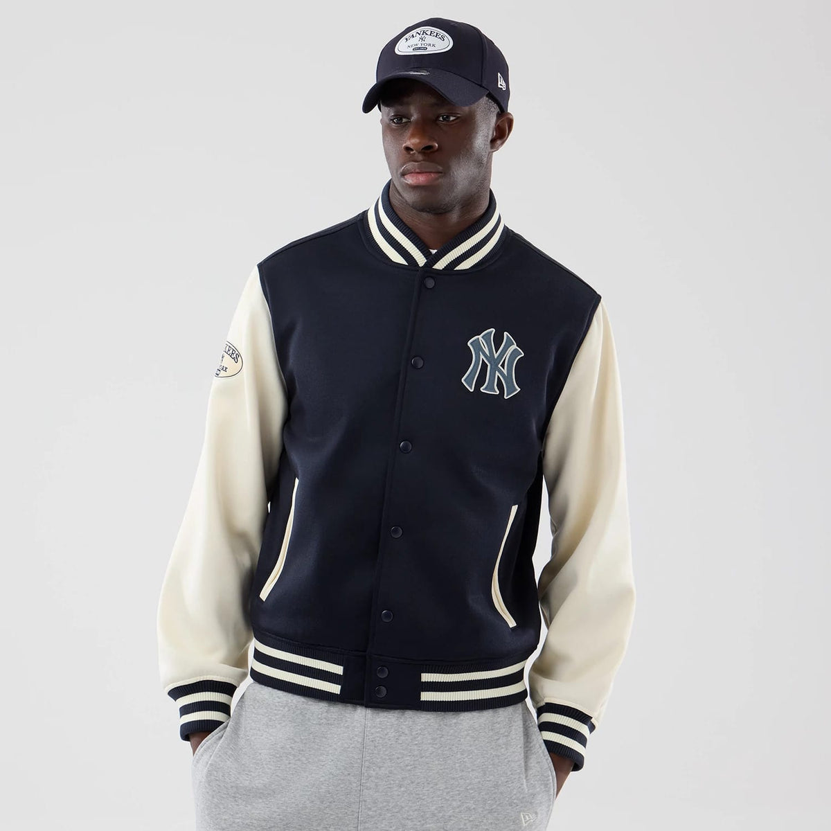 New Era New York Yankees MLB Jersey Bomber Navy Jacket, front view on-model showing the Yankees logo embroidered on the left chest, contrasting cream sleeves with a Yankees patch on the right shoulder, and striped cuffs and hem in navy and cream.