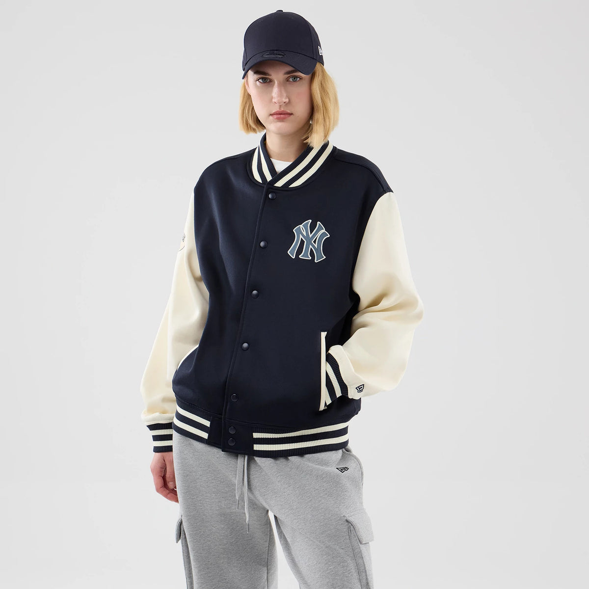 New Era New York Yankees MLB Jersey Bomber Navy Jacket, front view on a model showing the navy body with cream sleeves, embroidered NY logo on the left chest, striped ribbed cuffs and hem, and a debossed New Era flag logo on the left sleeve cuff.