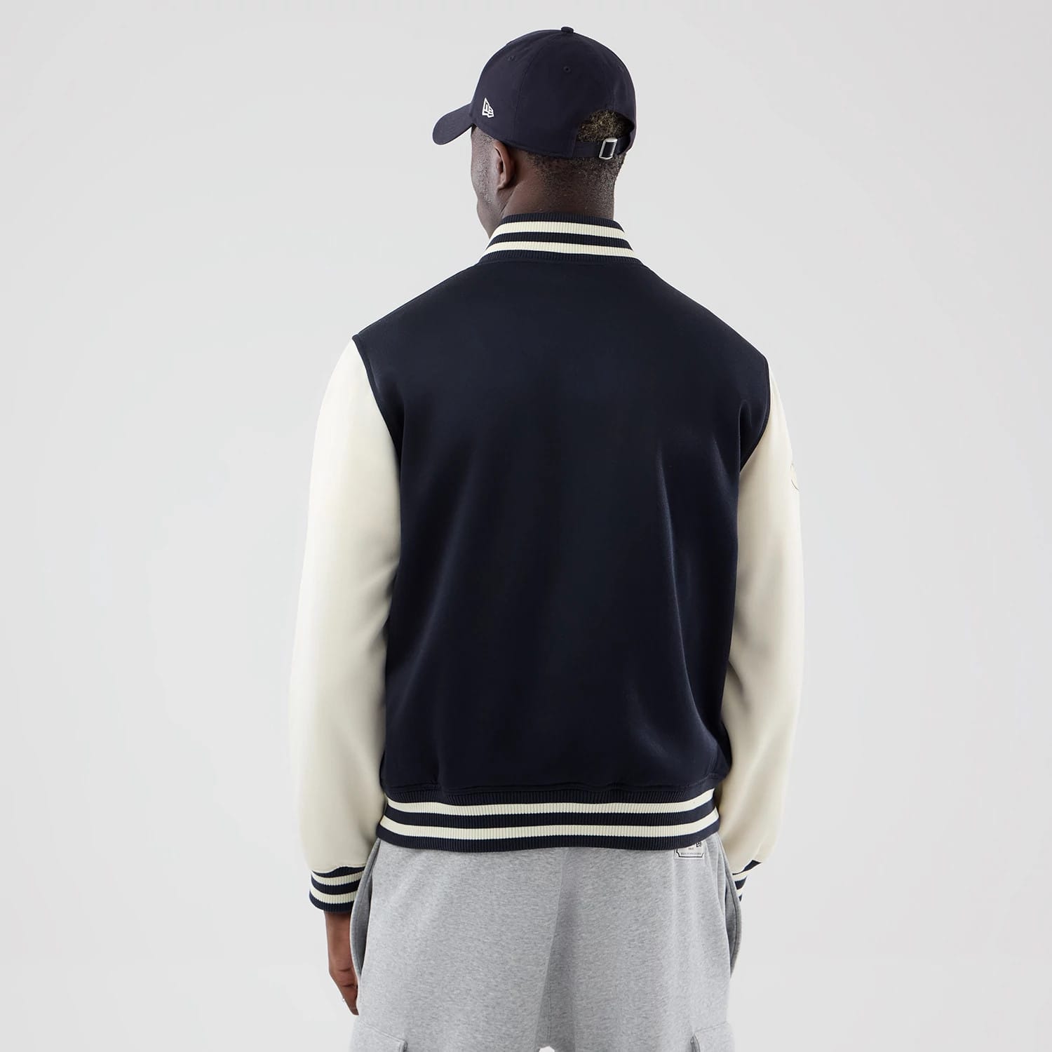 New Era New York Yankees MLB Jersey Bomber Navy Jacket, back view on a model with cream sleeves and a striped collar and cuff detail, displaying the navy back panel and New Era logo embroidered on the left sleeve, paired with a navy cap.