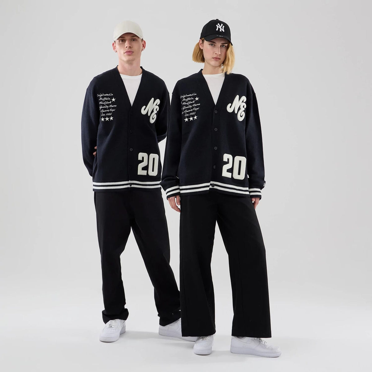 New Era Heritage Navy Cardigan, front view on two models styled with complementary black and white apparel, showing the white NE logo and script on the left chest, white 20 on the bottom right, and four white stars on the left.