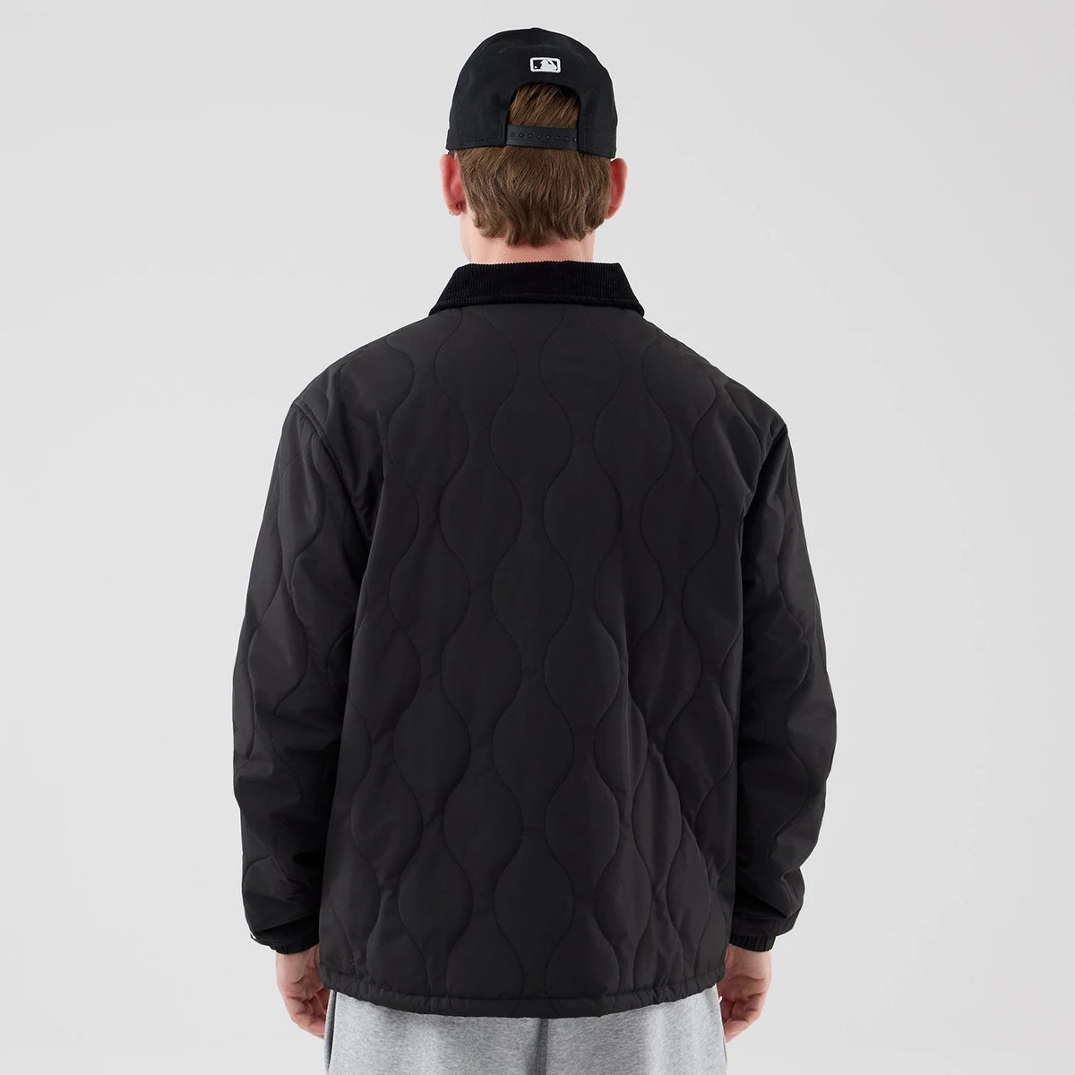 The model is wearing this New Era Quilted Coaches Jacket in black. 2