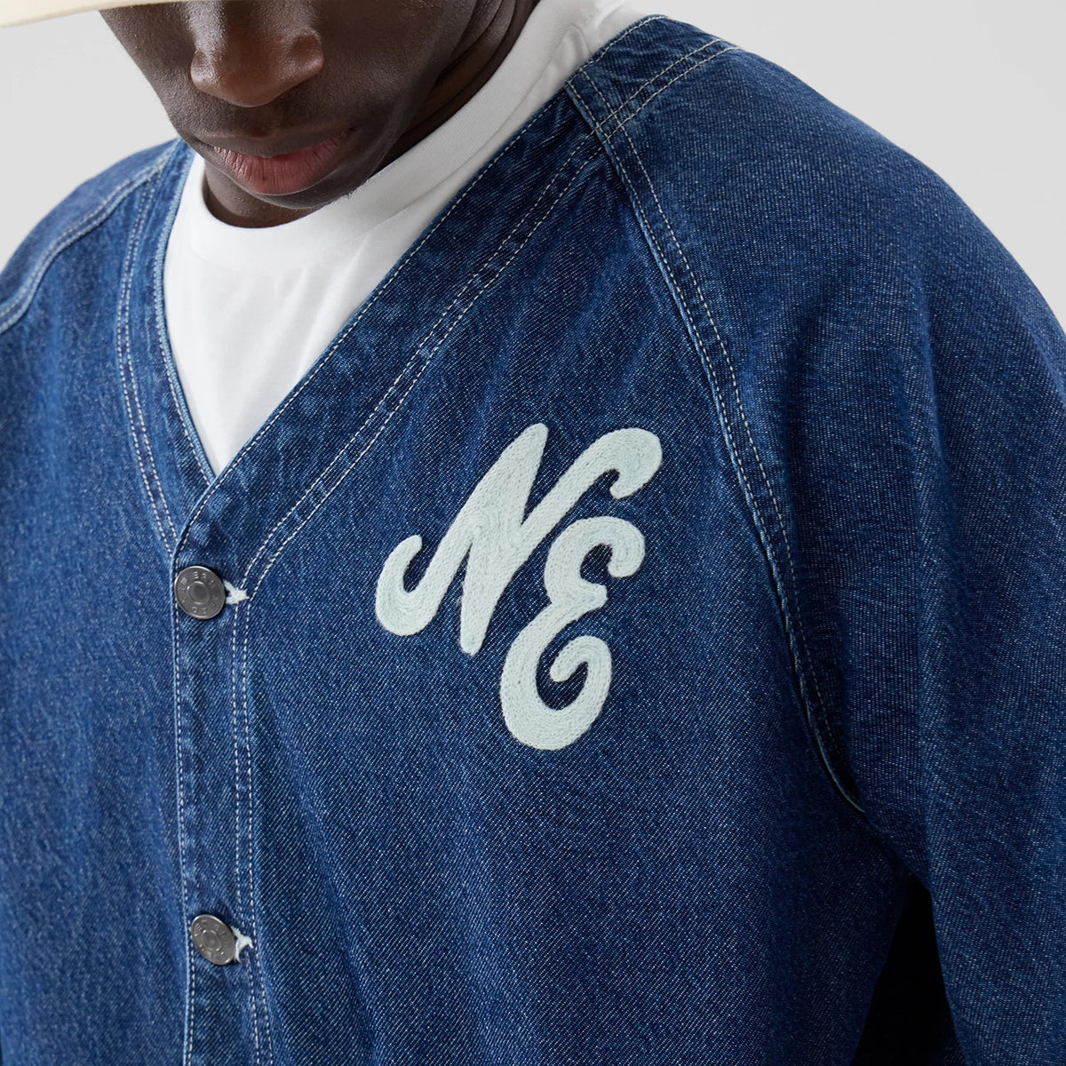 New Era Denim Dark Blue Worker Jacket, front view on-model showcasing the deep blue denim fabric with an embroidered white NE logo on the left chest, complemented by buttons down the front and prominent white stitching along the seams.