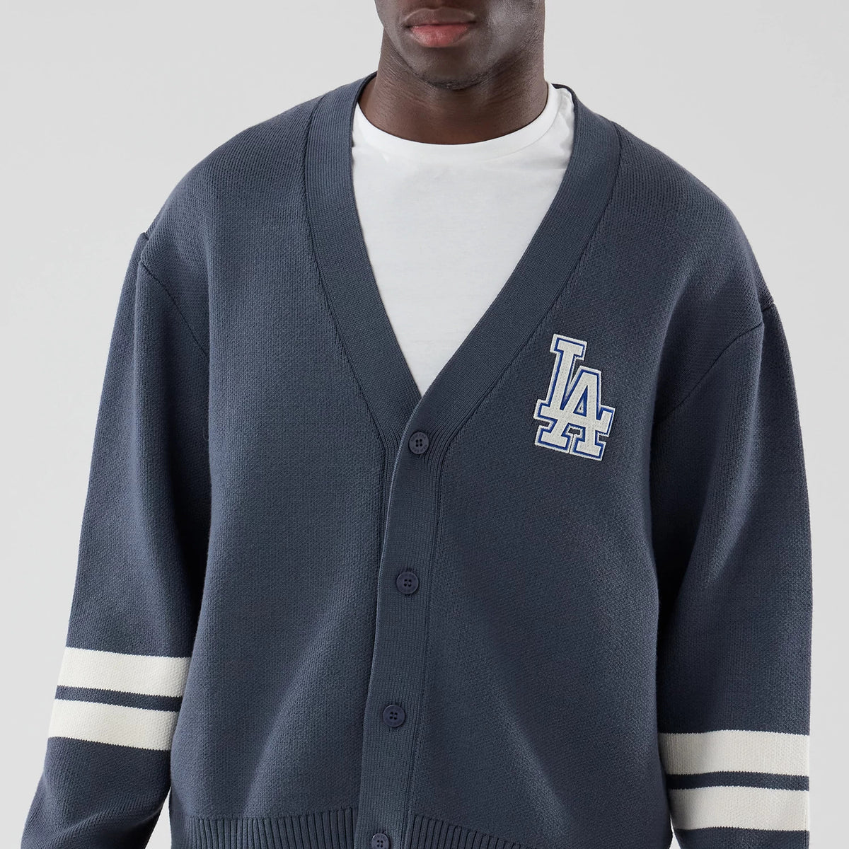 New Era LA Dodgers MLB Knit Grey Cardigan, front view on a model featuring a white embroidered LA logo on the left chest, a button-up front, and contrasting white stripe on the sleeves.