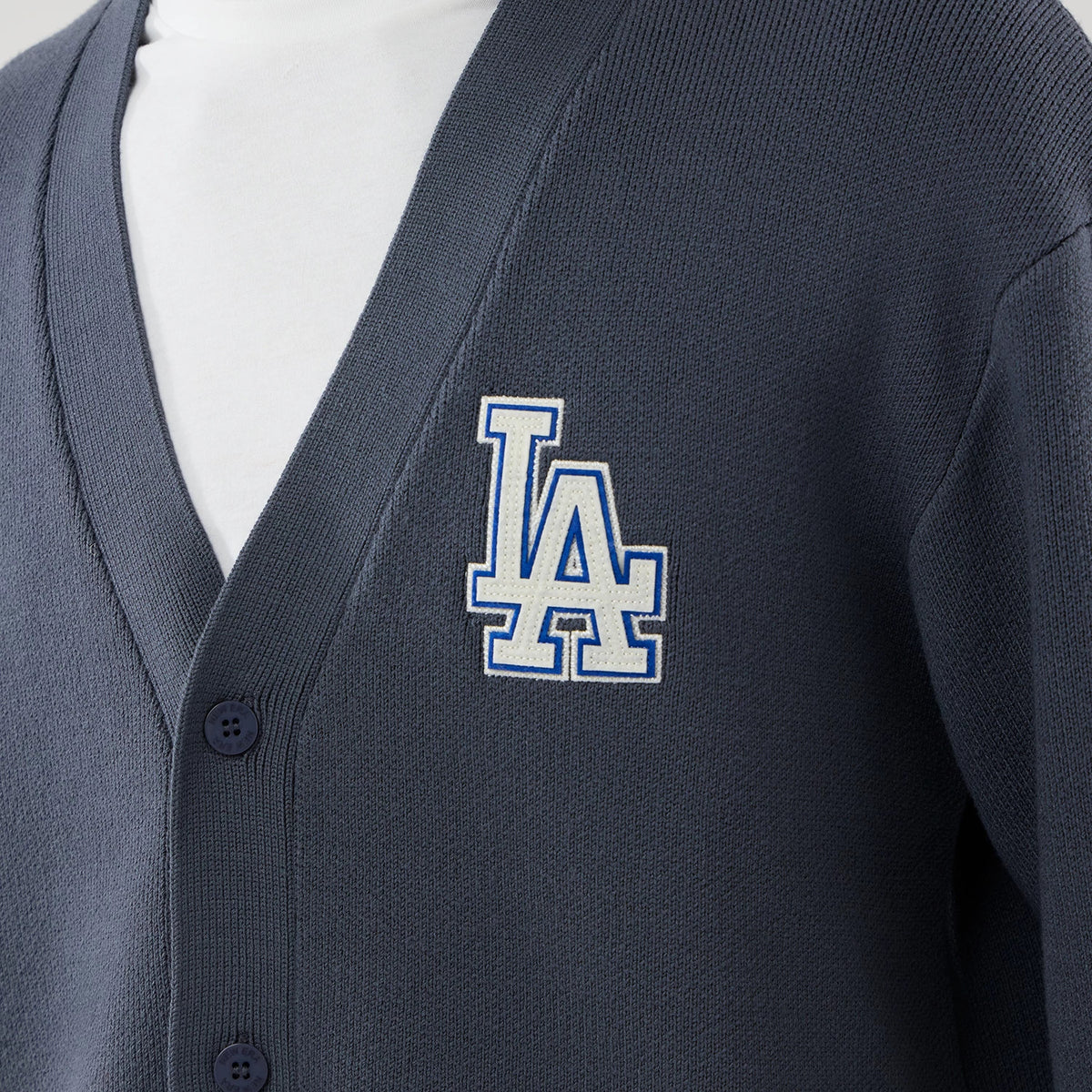 New Era LA Dodgers MLB Knit Grey Cardigan, front view showing a large embroidered white and blue LA logo on the left chest, with a ribbed texture and dark grey buttons along the placket, over a plain white garment.