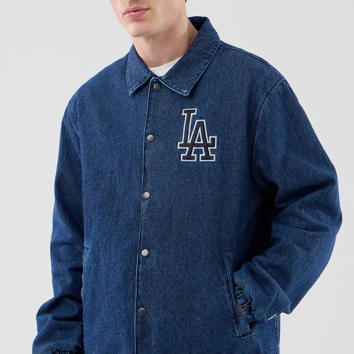 New Era LA Dodgers MLB Coaches Dark Blue Jacket, front view on-model showing the jacket with a prominent white embroidered LA logo on the left chest, a classic collar, and snap button closure, styled over a plain white T-shirt.