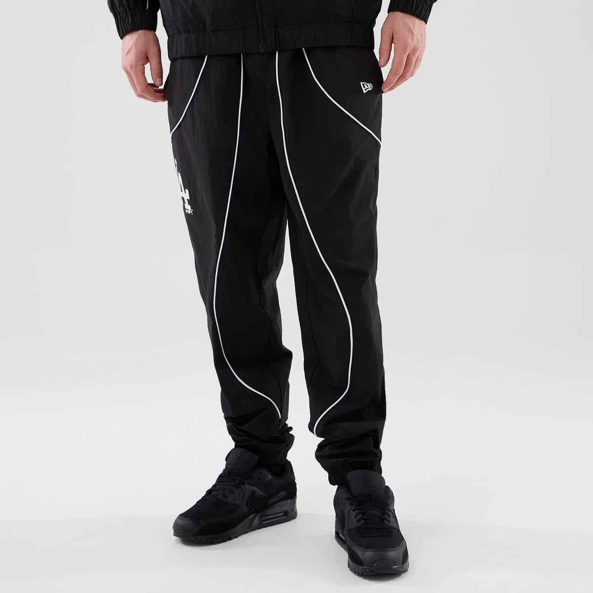 New Era LA Dodgers MLB Piping Track Black Track Pants, front view on a model with curved white piping along the legs, an embroidered New Era flag logo on the right thigh, and the LA Dodgers logo on the left thigh.