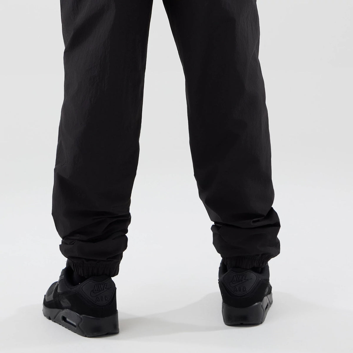 New Era LA Dodgers MLB Piping Track Black Track Pants, rear view showing elasticated cuffs at the ankles, straight-leg design, and black fabric, paired with black trainers for a sporty casual look.