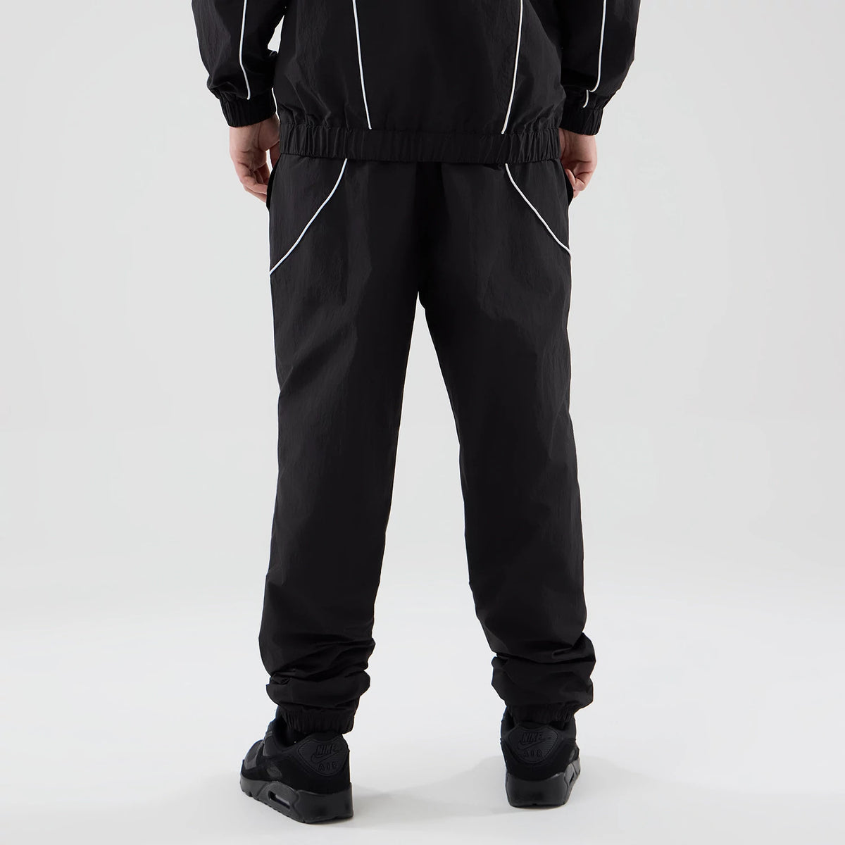 New Era LA Dodgers MLB Piping Track Black Track Pants, rear view on a model showing an elastic waistband, contrasting white piping along the pocket edges, and elasticated cuffs, all in a black fabric with a relaxed silhouette.