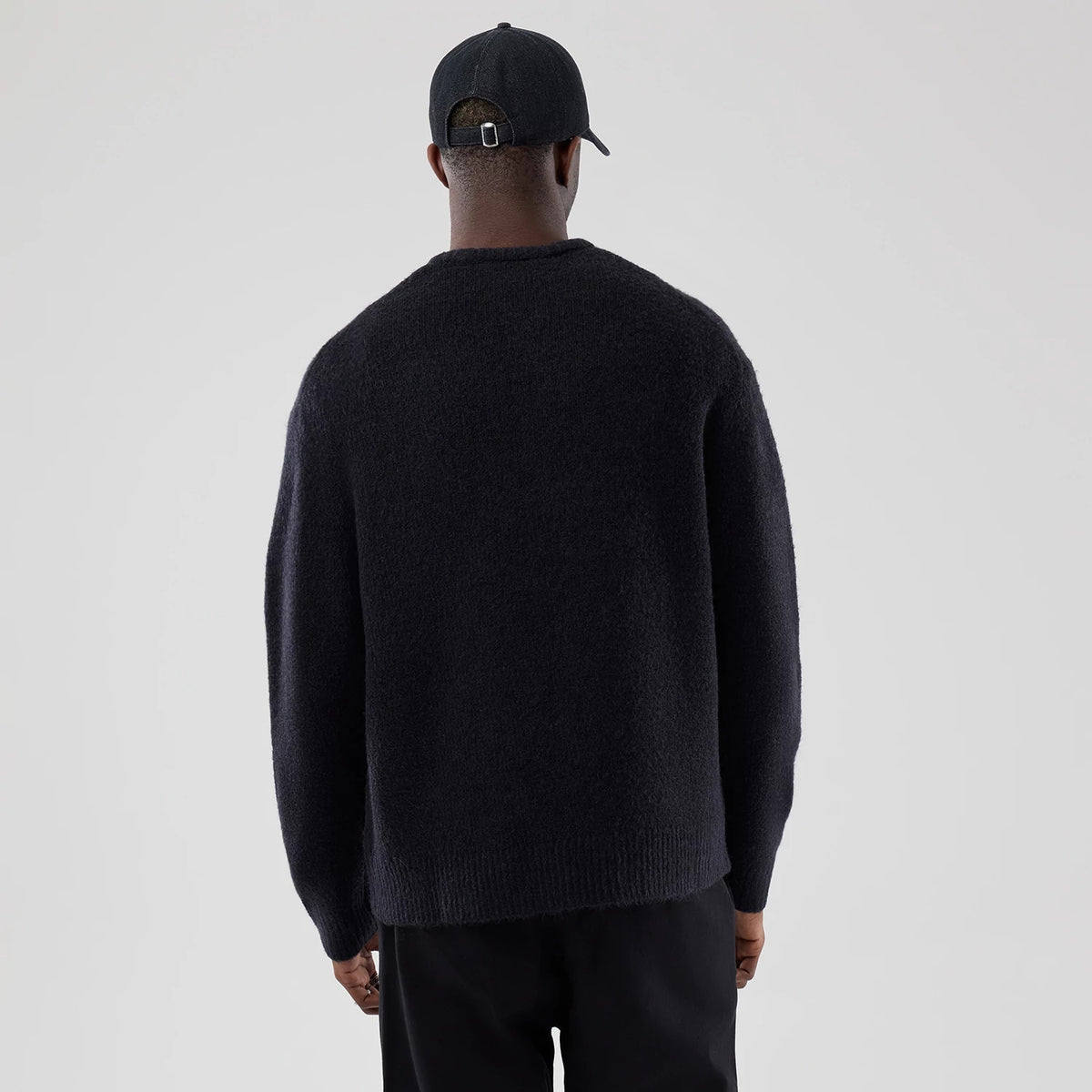 New Era Knit Heritage Navy Knitted Sweater, rear view on a model wearing a black cap, showing the rich navy texture of the sweater with a simple round neckline, loose fit and ribbed hem for a classic, timeless look.
