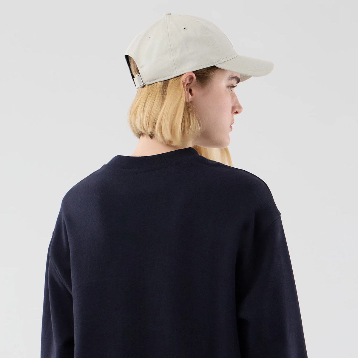 New Era New York Yankees MLB Arch Graphic Navy Oversized Crew Neck Sweater, rear view on a model wearing a beige cap, showcasing the sweater's simple navy back, relaxed fit and round neckline.