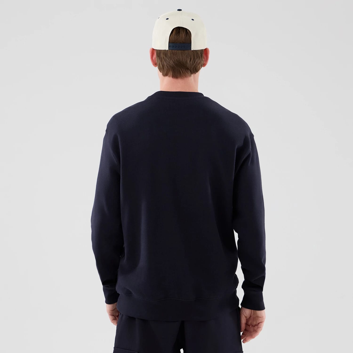 New Era New York Yankees MLB Arch Graphic Navy Oversized Crew Neck Sweater, back view on a model paired with a light-coloured cap, showing the sweater's simple navy design without any graphics, and a standard ribbed hemline.
